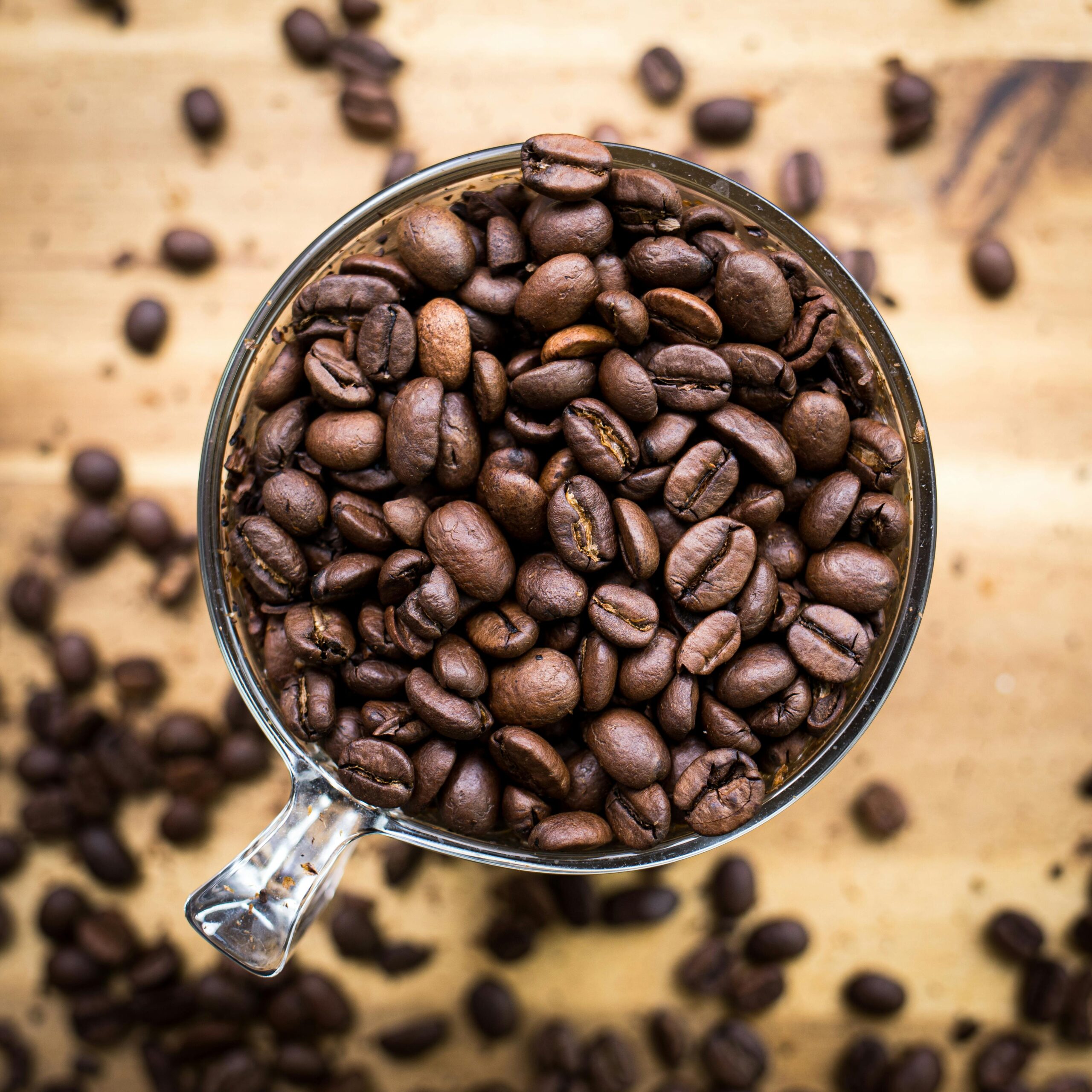 High-angle shot of coffee beans in a transparent cup on a wooden surface.