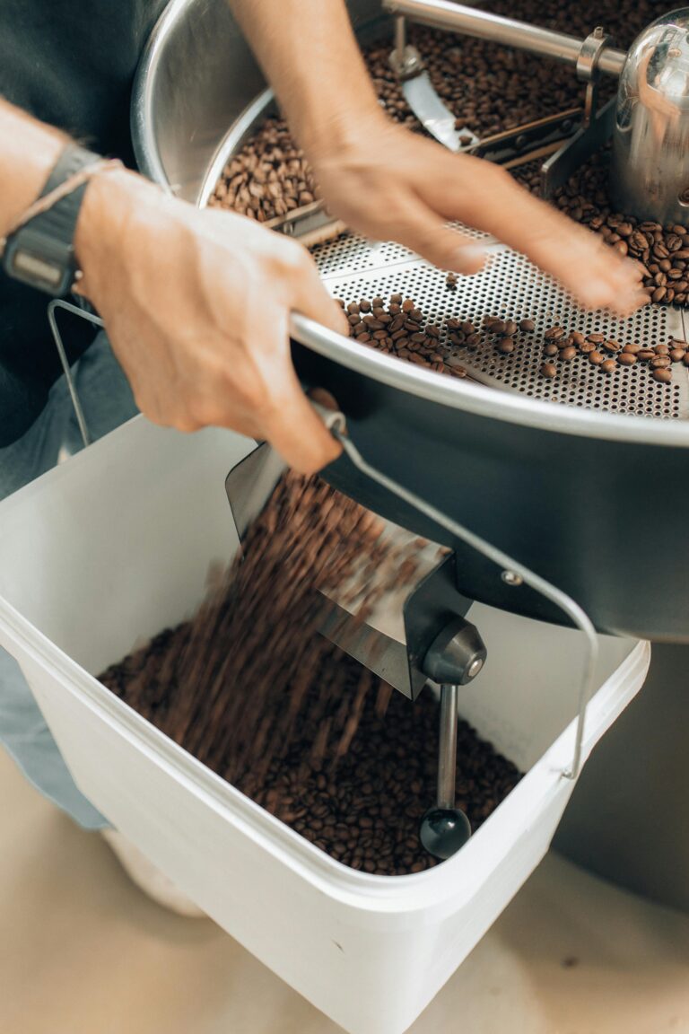 Close-up of hands handling roasted coffee beans in a modern coffee roaster.